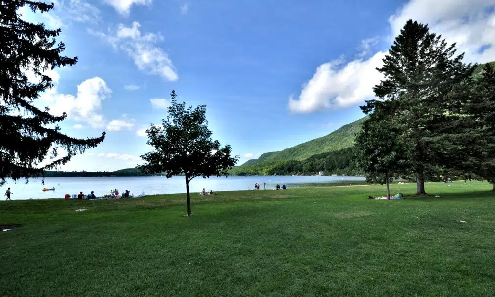 A group of people are sitting on a grassy area in a State Park near a lake.