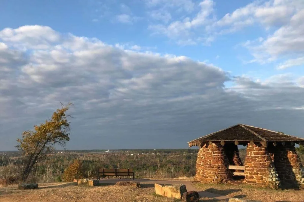 A stone gazebo at a State Park sits on top of a hill under a cloudy sky.
