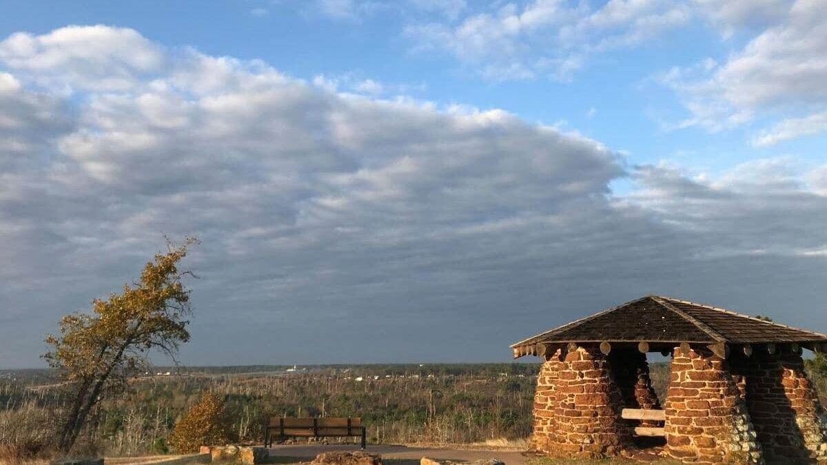 A stone gazebo at a State Park sits on top of a hill under a cloudy sky.