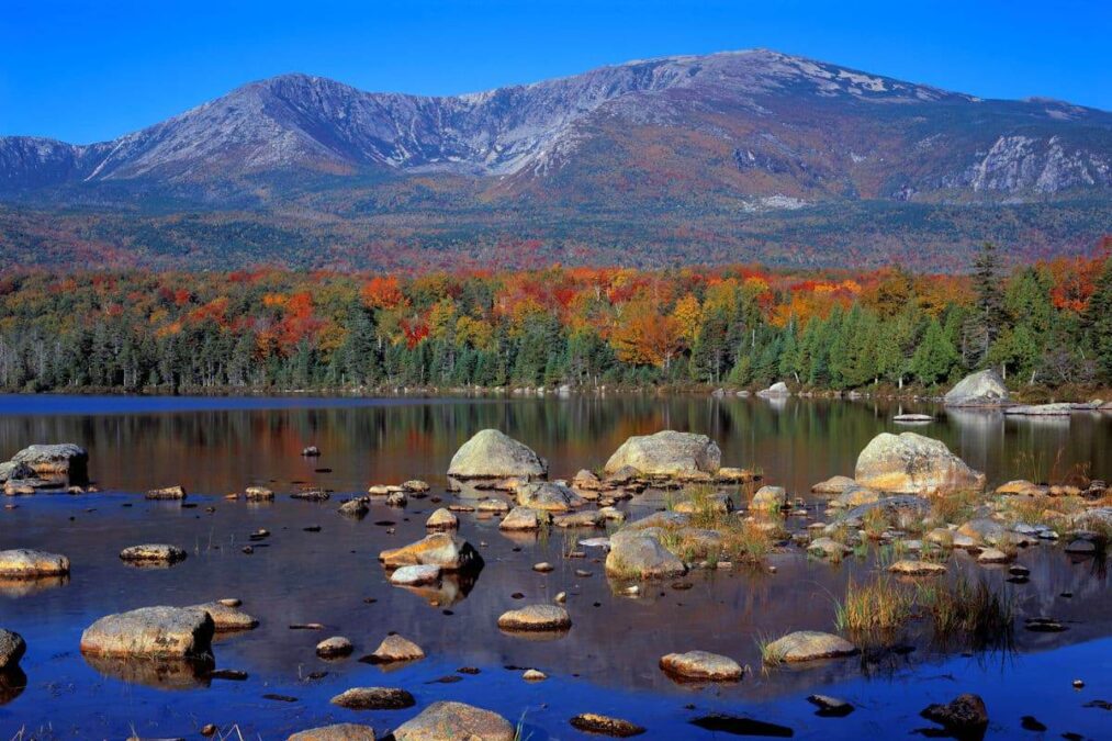 mountain rising above colorful trees surrounding lake at baxter state park in Maine