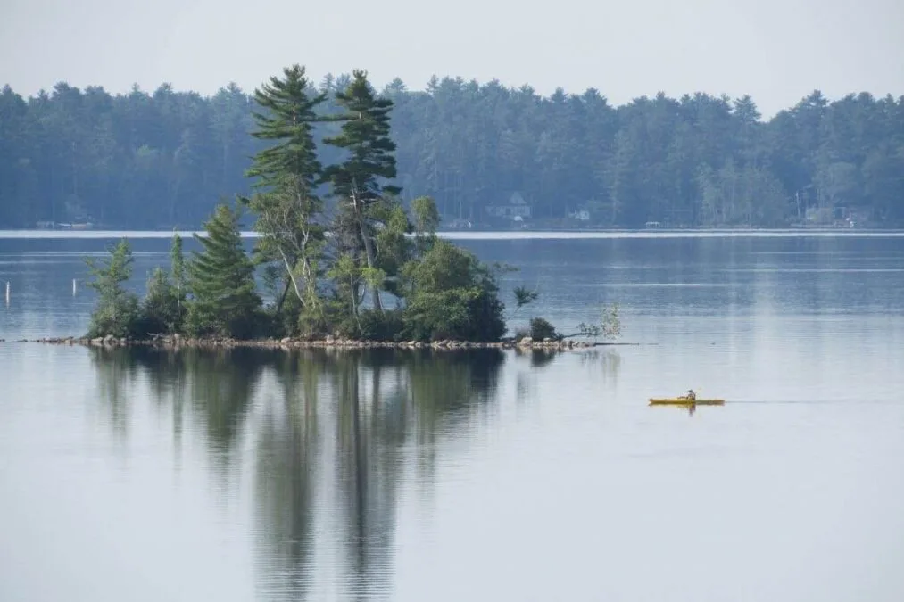View of Damariscotta Lake in Maine with a person on a kayak passing an island