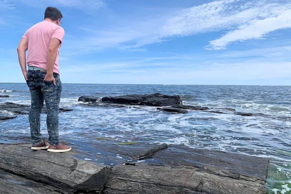Man looks at waves crashing against the coast at Two Lights State Park