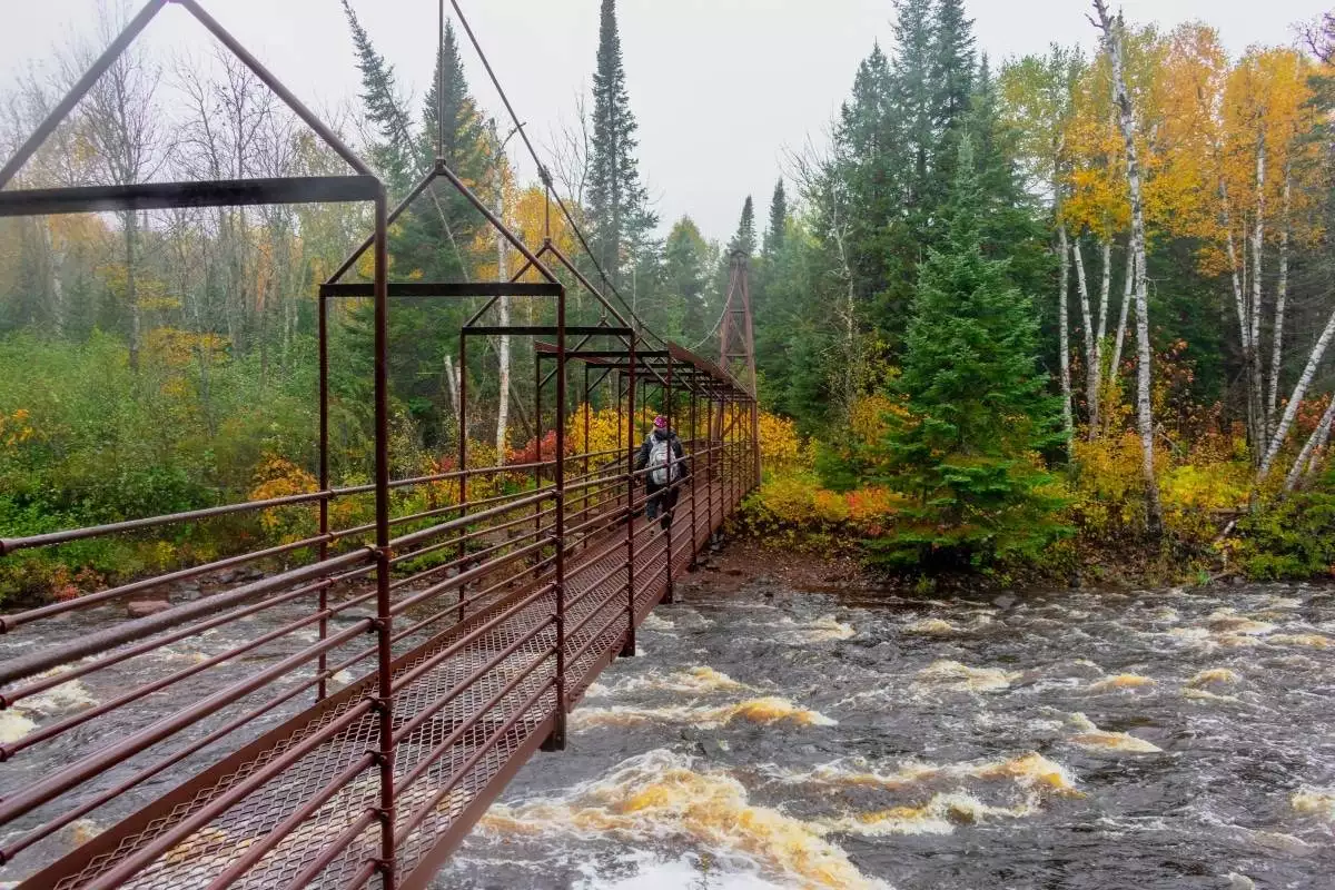 Woman hiking across suspension bridge over river at Tettegouche State Park