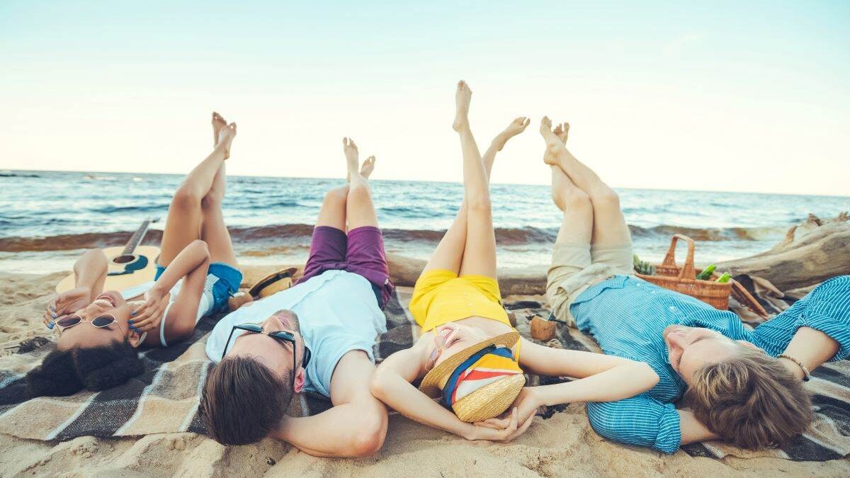 four people laying on a beach blanket on the sand at the beach