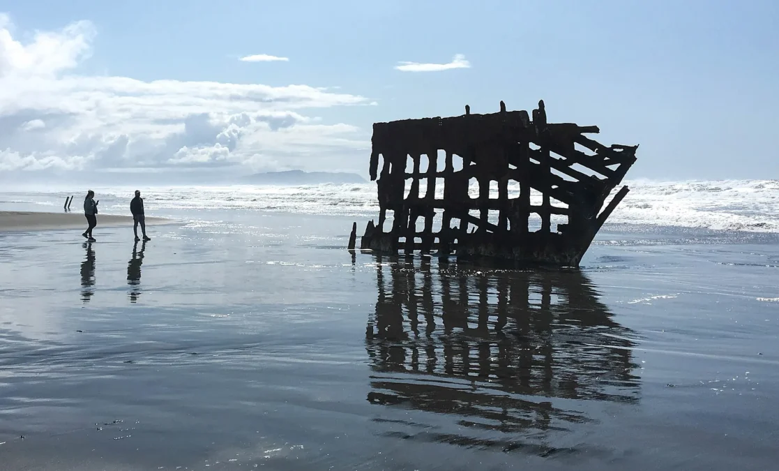 Fort Stevens State Park 57 Rusted wreck of the Peter Iredale on the wet beach with two walkers, Fort Stevens State Park, Oregon