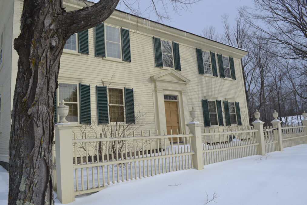 The Franklin Pierce Homestead, a two-story cream-colored Federal-style house with green shutters and a picket fence in winter