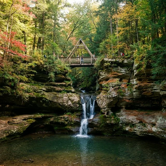 Old Man's Cave gorge at Hocking Hills with cascading waterfall, mossy sandstone walls, A-Frame bridge, and autumn foliage