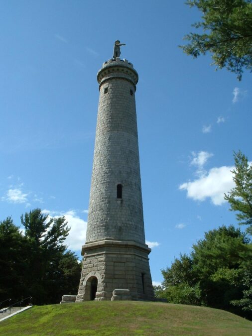 The granite Myles Standish Monument tower topped by a statue, rising above a grassy hill in Duxbury, Massachusetts